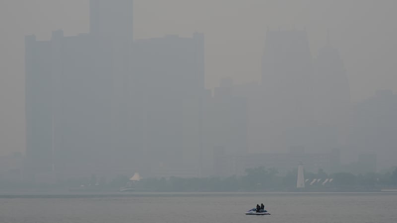 A watercraft sits in the Detroit River near the skyline during poor air quality due to smoke...
