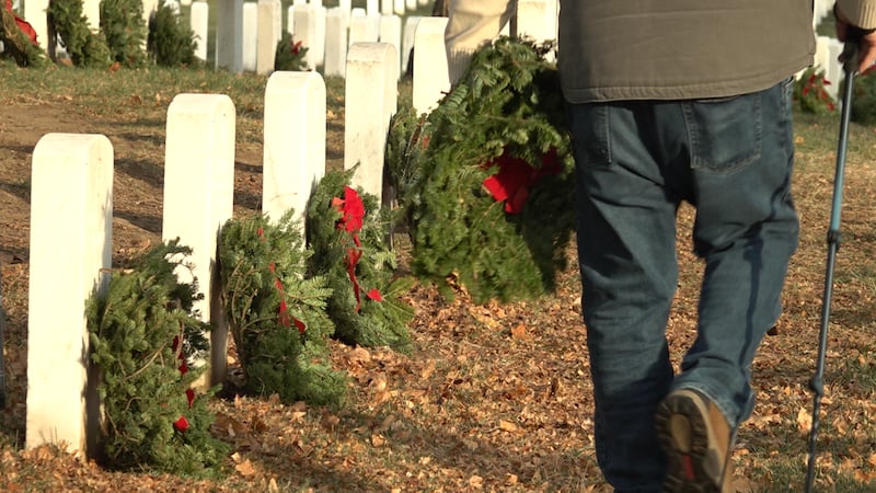 Someone walking past headstones with wreaths holding a wreath at Arlington National Cemetery...